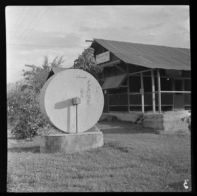 [Coconut oil mill wheel?], inscribed with [Japanese?] characters, in front Rabaul Branch of the Commonwealth Bank of Australia, New Britain, Papua New Guinea