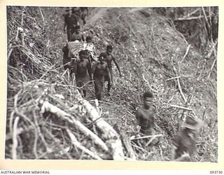 WEWAK AREA, NEW GUINEA, 1945-06-29. NATIVE BOYS CARRYING OUT A STRETCHER CASE PASSING OVER THE KNOLL AT THE FOOT OF HILL 2. STRETCHER PARTIES CARRY OUT WOUNDED OF THE 2/8 INFANTRY BATTALION ..