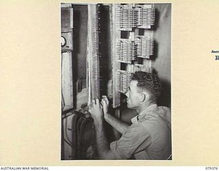 LAE, NEW GUINEA. 1945-03-11. A SIGNALLER OF NO.1 COMPANY, 19TH LINES OF COMMUNICATION SIGNALS USING A TEST SET, PORTABLE NO.2 MARK II WHILE CHECKING AND TESTING A NEWLY INSTALLED SWITCHBOARD FRAME