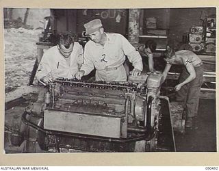JACQUINOT BAY, NEW BRITAIN. 1945-04-12. TECHNICAL SERGEANT J.F. FEROZ (1), AND LIEUTENANT B.C. BURKEHART (2), DISCUSSING REPAIRS TO A DIESEL BARGE ENGINE. IN THE BACKGROUND TWO MECHANICS ARE AT ..