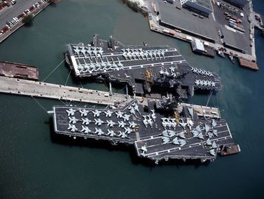 The aircraft carriers USS MIDWAY (CV-41), left and USS INDEPENDENCE (CV-62) lie tied up at the naval station. The MIDWAY is en route from Naval Station, Yokosuka, Japan, to Naval Air Station, North Island, California, where it will be decommissioned in the spring of 1992. The INDEPENDENCE will travel to Yokosuka to take over as the Navy's forward-based aircraft carrier