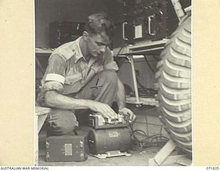 KATIKA, NEW GUINEA. 1944-03-31. NX65187 SIGNALMAN C. STRAHAN, B AUSTRALIAN CORPS SIGNALS, REPLACING A FUSE IN A GENEMOTOR OR DYNAMOTOR OF THE 188F, (UNITED STATES ARMY 191F), WIRELESS ..