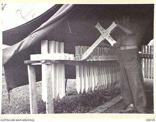CAPE MOEM, NEW GUINEA. 1945-10-23. OFFICIAL CROSSES IN THE STORE TENT, 7 WAR GRAVES UNIT, WAITING TO BE TRANSFERRED TO THE WAR CEMETERY. PRIVATE W.L. MARSHALL, IS PUTTING A CROSS IN THE RACK