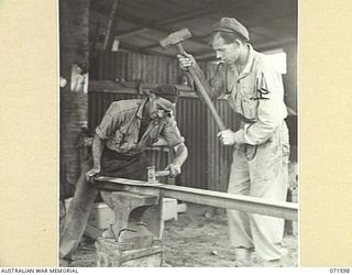 LABU POINT, LAE, NEW GUINEA. 1944-03-24. NX47123 CRAFTSMAN T. H. BROADBENT (LEFT), WITH VX26626 CRAFTSMAN L. S. MUSTEY (RIGHT), IN THE BLACKSMITH'S SHOP AT THE 1ST WATERCRAFT WORKSHOPS MAKING ..