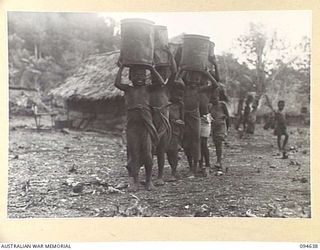 SIPILANGAN, NEW BRITAIN, 1945-07-30. NATIVE CHILDREN AT THE AUSTRALIAN NEW GUINEA ADMINISTRATIVE UNIT DISTRICT SERVICES TOL REFUGEE CAMP, LEARN EARLY TO CARRY THINGS ON THEIR HEADS. HERE THEY ARE ..