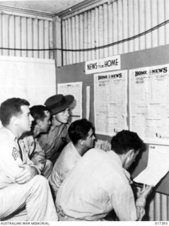 New Guinea. 1944. The Department of Information's wall newspaper "Home News" was of interest to Australians and Americans alike. Studying it are Sergeant W. C. Rinker of Tiffin, Ohio, Private First ..