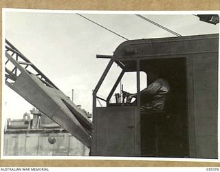 LAE, NEW GUINEA, 1943-11-05. TECHNICAL SERGEANT E.D. HANSON OF THE 1052ND ENGINEERS PORT CONSTRUCTION AND REPAIR GROUP, UNITED STATES ARMY OPERATING A CRANE, DURING THE CONSTRUCTION OF THE FIRST ..