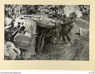 ALEXISHAFEN, NEW GUINEA. 1944-05-12. A MEMBER OF HEADQUARTERS 8TH INFANTRY BRIGADE EXAMINING AN OVERTURNED JAPANESE TRUCK ON THE ROAD TO MUGIL HARBOUR. THE TRUCK WAS LATER RECOVERED AND DRIVEN TO ..