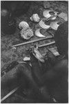 Ritual exchange, Tsembaga: man examines shell valuable, steel axes and other shells in background