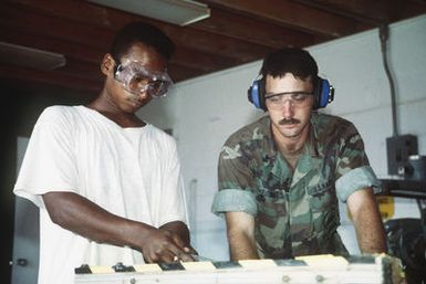 Equipment Operator Second Class (EO2) Larry Fulbright instructs one of several local workers in the basic functions of carpentry. The Seabees operate an apprenticeship program with the local labor force to aid in training for self-help programs