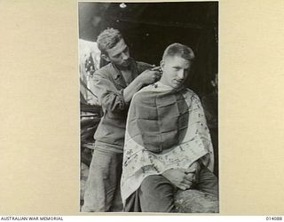 1943-01-14. PAPUA. BUNA. SILKEN JAPANESE FLAG IS USED AS A BARBER'S TOWEL. BARBER IS CPL. L. LOBADA OF DETROIT, MICHIGAN. HIS CUSTOMER IS FIRST/LIEUT. W.A. SIKKEL OF HOLLAND, DETROIT, MICHIGAN. ..