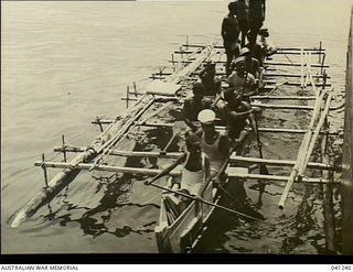 Los Negros Island, Admiralty Group. c. 1943. A group of natives in a large outrigger canoe alongside HMAS Broome