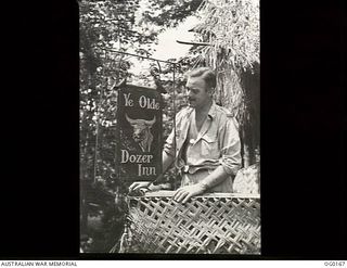 VIVIGANI, GOODENOUGH ISLAND, PAPUA NEW GUINEA. 1943-09-23. FLYING OFFICER J. W. MCENIRY, BENDIGO, VIC, ADJUTANT, ADMIRING HIS HANDIWORK, THE SIGN AT THE ENTRANCE TO THE OFFICER'S MESS AT NO. 7 ..