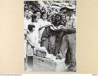 RATONGOR, NEW BRITAIN, 1945-09-18. AFTER THE SURRENDER OF THE JAPANESE, RED CROSS REPRESENTATIVE A. SCOFFORD, IS SEEN HANDING OUT CLOTHING TO CHINESE WOMEN INTERNEES, WHO WERE OVERJOYED WITH THE ..