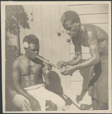 Aiau, the Chinnery's garden boy, lighting a bamboo pipe for Asavia, Malaguna Road, Rabaul, New Guinea, ca. 1936 / Sarah Chinnery