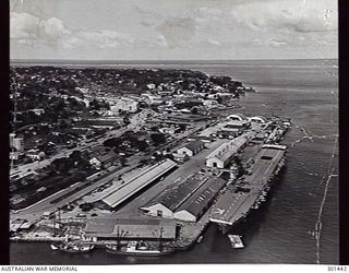 1956-08-25. SUVA, FIJI. AERIAL BOW VIEW OF THE AIRCRAFT CARRIER HMAS SYDNEY (III), NOW OPERATING AS THE FLEET TRAINING SHIP, ALONGSIDE. NOTE THE POSITIION OF THE LIFTS, BOTH OF WHICH ARE RETRACTED. ..