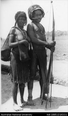 Man carrying bow and arrows and woman in grass skirt carrying bags