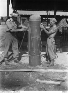 NX91452 Lieutenant A. L. S. Minkie (1) and Warrant Officer I. A. Brun (2) of the Solomon’s Detachment 12th Air Maintenance Platoon (TS), 4th Base Sub Area, roping a storepedo ( a cylindrical ..