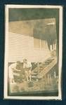 Kath Honeysett and Tony playing with a dog in front of stairs leading to house, rose garden in foreground, New Guinea, c1932 to 1933