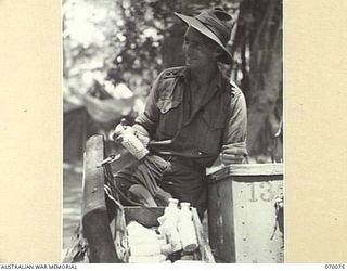 GOALING RIVER AREA, WEST NEW GUINEA. 1944-01-25. WX9409 LIEUTENANT R. A. J. HALL OF THE 9TH DIVISION SALVAGE UNIT, HOLDING BOTTLES OF JAPANESE QUININE TABLETS BESIDE AN OPEN BOX OF ABANDONED ..