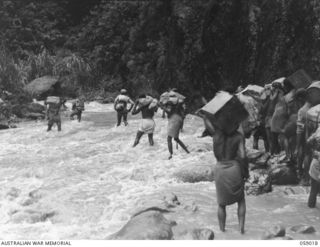 FARIA VALLEY, NEW GUINEA, 1943-10-17. NATIVE CARRIER TRAIN CROSSING THE FARIA RIVER ON THEIR WAY TO JOHN'S KNOLL, WITH SUPPLIES ON THEIR SHOULDERS, FOR THE 2/16TH AUSTRALIAN INFANTRY BATTALION