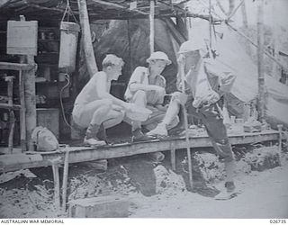 PAPUA. 1942-09. AN AUSTRALIAN ARMY AMBULANCE POST IN THE OWEN STANLEY RANGE BUILT WITH BUSH TIMBER. A SOLDIER IS HAVING MEDICAL TREATMENT FOR A LEG WOUND