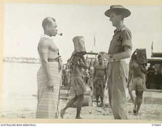 ALEXISHAFEN NORTH, NEW GUINEA. 1944-09-01. NX120697 LIEUTENANT S.J. OSBORN, MILITARY LANDING OFFICER, 241ST SUPPLY DEPOT PLATOON (2) GIVING INSTRUCTIONS TO BUDUB (1) BOSS BOY IN CHARGE OF A GANG OF ..