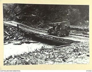 DUMPU AREA, NEW GUINEA. 1944-04-18. A JEEP DRIVEN BY A MEMBER OF THE 15TH FIELD COMPANY, ROYAL AUSTRALIAN ENGINEERS CROSSING THE BRIDGE OVER THE FARIA RIVER ON THE NEW ROAD. THE FOOT BRIDGE IN THE ..