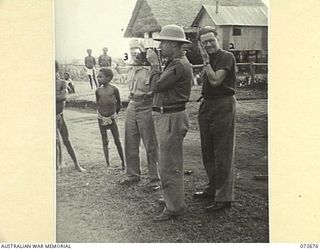 HIGITURA, NEW GUINEA. 1944-04-27. MR J. DONOVAN, PRIVATE SECRETARY TO THE MINISTER (1), PHOTOGRAPHS A GROUP OF NATIVE DANCERS, WATCHED BY THE HONOURABLE E.J. WARD, MINISTER FOR EXTERNAL TERRITORIES ..