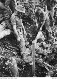 TROOPS OF THE 2/16TH AUSTRALIAN INFANTRY BATTALION, 21ST AUSTRALIAN INFANTRY BRIGADE, UNEARTH A DEAD JAPANESE SOLDIER ON THE "PIMPLE" AFTER THE BATTLE. IDENTIFIED PERSONNEL ARE: WX5607 LIEUTENANT ..