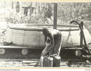 JACQUINOT BAY, NEW BRITAIN. 1944-11-20. A NATIVE FILLING WATER CANS FROM A 1200 GALLON CANVAS WATER TANK ERECTED BY MEMBERS OF THE 9TH FIELD COMPANY