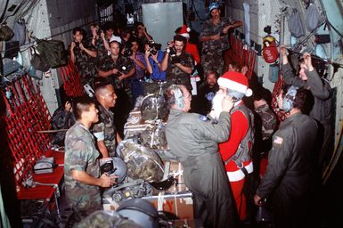 An airman dressed as Santa is assisted with his helmet as he prepares to push boxes rigged with parachutes out the back of a 374th Airlift Wing C-130 Hercules aircraft to islanders of the Federated States of Micronesia. Flown by crews from the 345th and the 21st Airlift Squadrons, the C-130 is participating in Christmas Drop '92, the 40th anniversary of the humanitarian effort. Every Christmas since 1952, food, clothing, tools and toys donated by residents of Guam have been delivered by air to 40 Micronesian islands