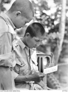LAE, NEW GUINEA. 1944-12-30. TWO JAPANESE PRISONERS OF WAR INTERESTEDLY READING THE CARD ISSUED TO THEM BY THE AUSTRALIAN RED CROSS SOCIETY REPRESENTATIVE BEFORE GIVING THEM A PARCEL OF COMFORTS. ..