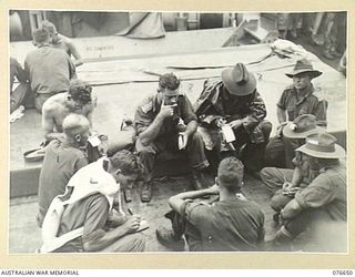 AT SEA. 1944-11. OFFICERS OF B COMPANY, 14/32ND INFANTRY BATTALION CHECKING FINAL DETAILS OF THEIR COMPANY LANDING AT JACQUINOT BAY THE FOLLOWING MORNING. IDENTIFIED PERSONNEL  LEFT TO RIGHT AROUND ..