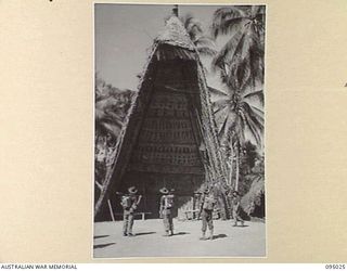 SAIGORA, NEW GUINEA, 1945-08-05. TROOPS OF 2/7 INFANTRY BATTALION PAUSE IN THE MAIN STREET OF THE VILLAGE TO VIEW THE PORTALS OF A NATIVE TAMBORAN (HOUSE OF KNOWLEDGE AND WORSHIP). THE MEN ARE ON A ..