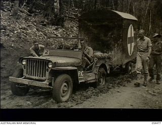 New Guinea. 1943-07-20. A jeep experiencing problems in towing an ambulance trailer through mud on the road between Skindewai and Barara Staging Camps
