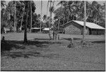 Village scene: church building (r), people carry bundles on heads