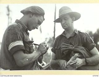 NORTH ALEXISHAFEN, NEW GUINEA. 1944. THE COURIER OF THE 5TH AUSTRALIAN DIVISION SIGNALS (RIGHT) PREPARES TO HAND OVER LETTERS AND ORDERS TO A SIGNALLER FROM HEADQUARTERS, 8TH AUSTRALIAN INFANTRY ..