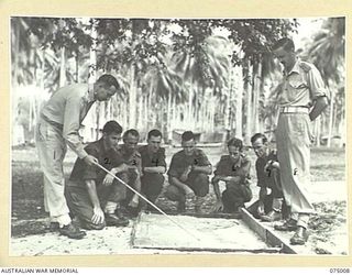 MILILAT, NEW GUINEA. 1944-08-01. NX116896 CAPTAIN G.C. AYRTON, INTELLIGENCE OFFICER (1) LECTURING MEMBERS OF HEADQUARTERS, 5TH DIVISION INTELLIGENCE SECTION WITH THE ASSISTANCE OF A SAND MODEL OF ..