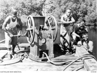 Jacquinot Bay, New Guinea. 1945-03. Natives working the pumps for Australian sappers who improvised diving helmets from gas masks while building a shipway for barge repairs