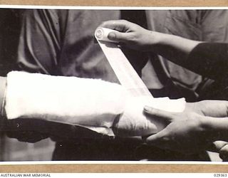 FORBES, AUSTRALIA. 1943-02. BANDAGING THE ARM OF A "GUINEA PIG" WHO, WHILE TAKING PART IN GAS SHELL EXPERIMENTS, INDULGED IN UNAUTHORISED EXPERIMENTS OF HIS OWN. THE INJURY TO THE ARM IS SHOWN IN ..