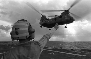 A flight deck crewman signals to a CH-46 Sea Knight helicopter as it takes off from the amphibious assault ship USS GUAM (LPH 9), during operations off the coast of Beirut, Lebanon