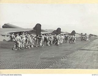 1943-09-15. LINED UP BEHIND THE GIANT TRANSPORT PLANES. WHICH CARRIED THEM TO THE MARKHAM VALLEY AMERICAN PARATROOPS AND AUSTRALIAN AIRBORNE ARTILLYMEN HAVE A FINAL CHECK OVER OF THEIR PARACHUTES ..