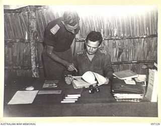 CAPE WOM, NEW GUINEA. 1945-09-29. LIEUTENANT R.W. GRUBB (1) AND CAPTAIN A.J.A. NELSON (2), AUSTRALIAN ARMY EDUCATION SERVICE OFFICERS, AT HEADQUARTERS 6 DIVISION DISCUSSING ADMINISTRATION