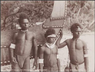 Three young men standing in front of a painted canoe at Heuru, Solomon Islands, 1906 / J.W. Beattie