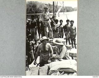 NEW GUINEA, 1942-08-03. AMERICANS MAN A RUBBER BOAT COMING DOWN A RIVER IN NEW GUINEA WITH ITS CARGO WHILST THE NATIVE WORKMEN STAND BEHIND