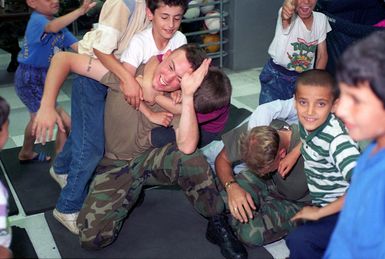 Marines from Bravo Company, First Battalion, Sixth Marines, play with Kurdish evacuee children in the recreation center at Tiyan, Guam, during Marine Joint Task Force Operation PACIFIC HAVEN. Marine Forces provide many recreational activities for the evacuees during their stay on Tiyan. PACIFIC HAVEN provided Kurdish evacuees political asylum from Iraq. While on Guam, the Kurds are provided shelter, food, clothing, medical care and assimilation classes for life in the United States