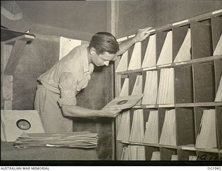 MADANG, NEW GUINEA. C. 1944-10. 435397 SERGEANT F. E. SHEPPARD, BRISBANE, QLD, FORMERLY ANNOUNCER AND REGIONAL OFFICER FOR THE AUSTRALIAN BROADCASTING COMMISSION IN QUEENSLAND SELECTING A RECORD ..