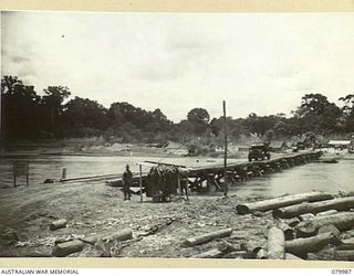 TOKO-BARARA ROAD, BOUGAINVILLE, SOLOMON ISLANDS. 1945-03-28. MEMBERS OF THE 15TH FIELD COMPANY, ROYAL AUSTRALIAN REGIMENT WATCH A 3 TON VEHICLE LOADED WITH TOP DRESSING CROSS THE PUIATA RIVERT ON ..