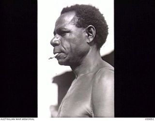 BUKAUA, NEW GUINEA. 1943-10-18. PORTRAIT OF YUMSA SMOKING A CIGARETTE, A VOLUNTEER FOR THE AUSTRALIAN AND NEW GUINEA ADMINISTRATION UNIT LABOUR FORCE